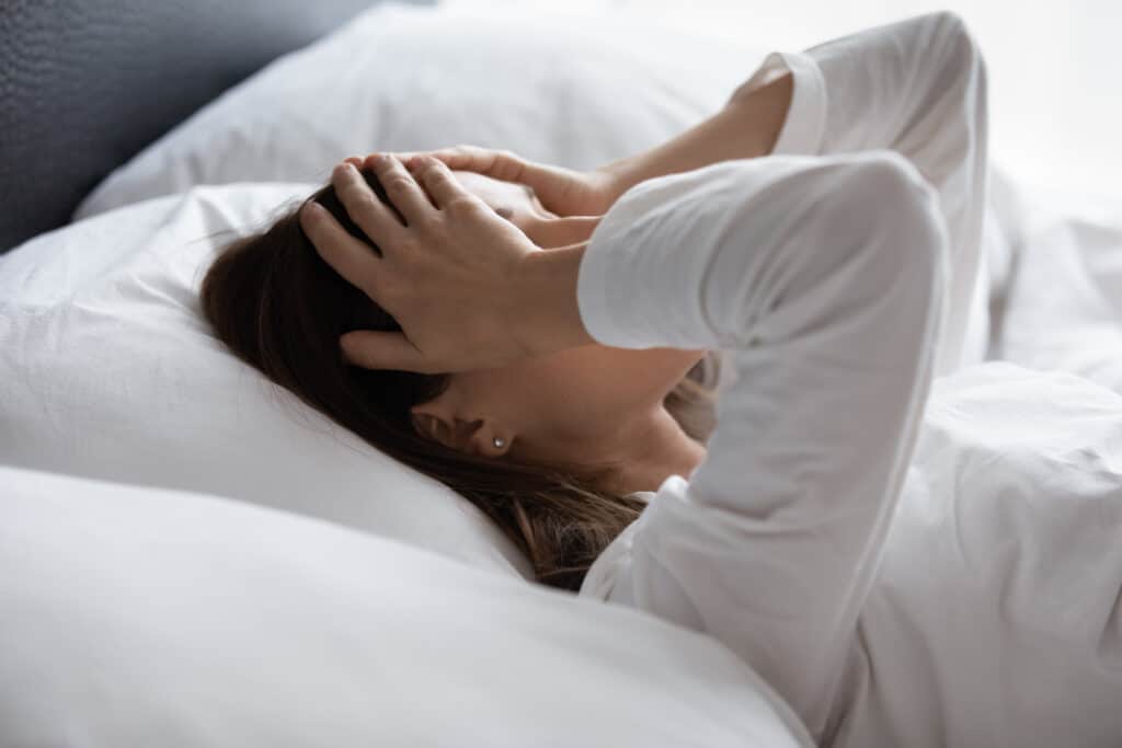A woman lying in bed covering her eyes