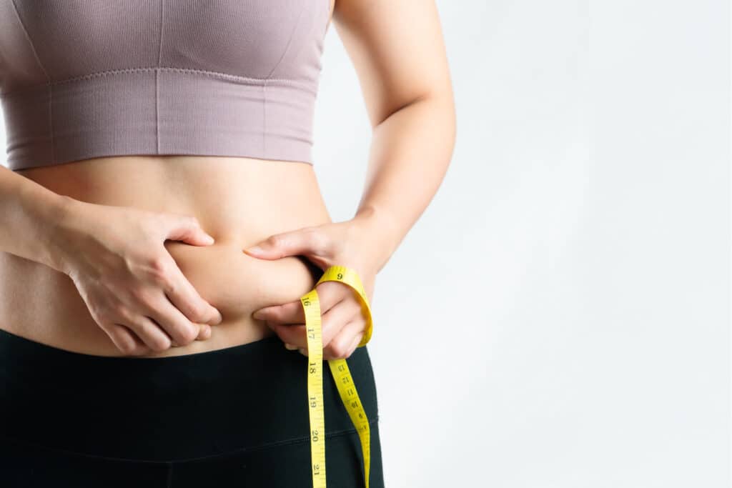 A woman pinching the fat on her stomach and holding a tape measure before Sermorelin and Tesamorelin treatment