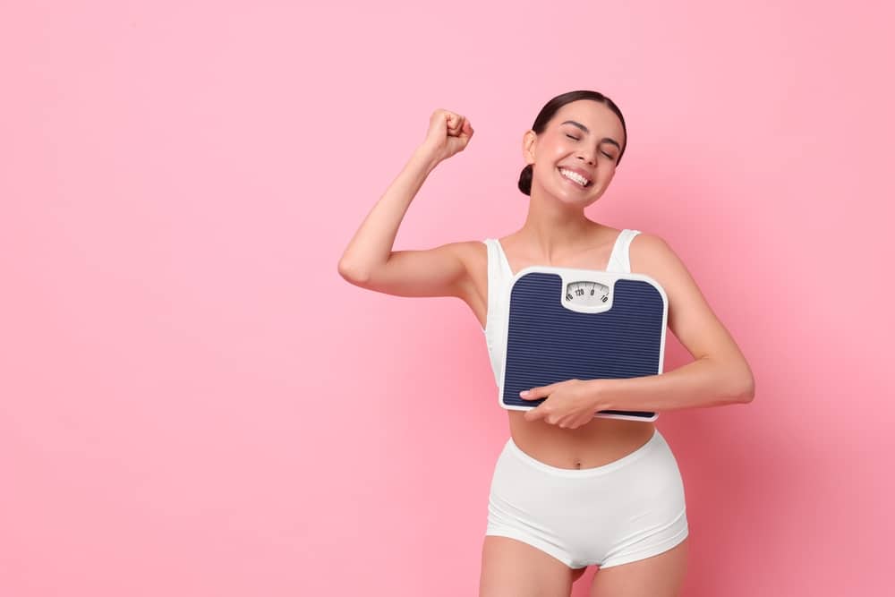 A woman holding a scale and smiling after losing weight with semaglutide